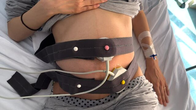 Beautiful young pregnant woman at electrocardiogram checkup for baby health and expected date of birth. Fetal heart monitoring. Healthcare and medical service concept. Top view, natural light, 4K UHD.