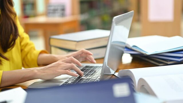Side view of college students hands typing on keyboard of laptop, studying for school assignment in library