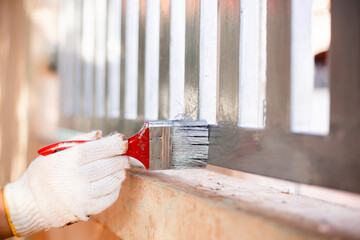 Human hand painting a house fence, doing home improvement by refreshing the paint of the steel fence. Close-up  hand wearing glove and holding brush. Fresh wet silver paint.