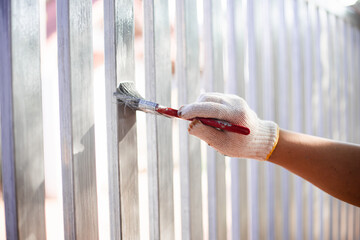 Human hand painting a house fence, doing home improvement by refreshing the paint of the steel...