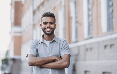 Naklejka na ściany i meble Young man in a city looking at camera, Confident businessman with crossed arms smiling outdoor, Handsome student men summer portrait, People lifestyle, city life, casual business concept