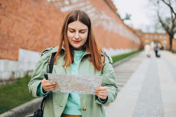 Happy optimistic woman smiling confident holding city map at street. Attractive young female tourist is exploring new city. Traveling Europe in spring. Urban lifestyle banner