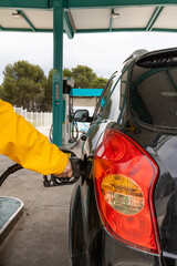 detail of gloved hand putting petrol with petrol pump, man in yellow raincoat black car sub large