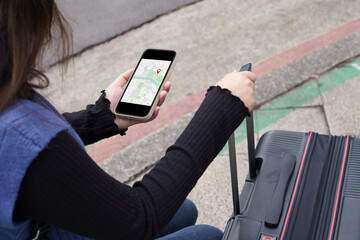 Woman with baggage in downtown city street searching location in map application online on smart...