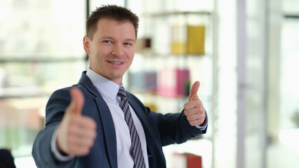 Happy smiling businessman showing thumbs up gesture in office. Successful career growth in business concept