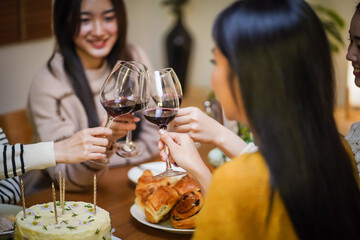 Cheerful friends enjoying home Birthday holiday party. Asian Friends cheering drinking red wine celebrating Christmas or New Year party