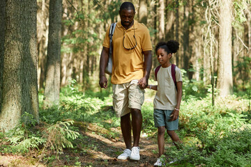 African American dad walking along the footpath with his daughter in the forest during their travelling on the nature