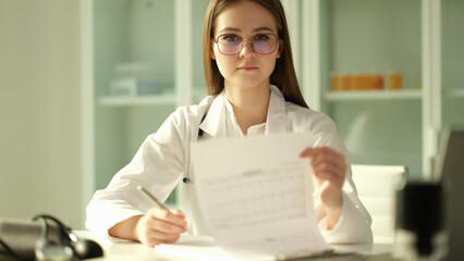Doctor cardiologist examining patient cardiogram on paper in clinic. Diagnosis of heart disease...