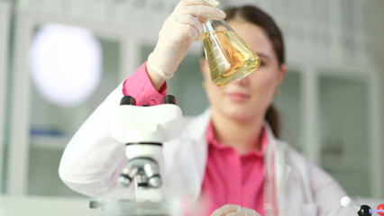 Scientist chemist looking at flask with yellow liquid or oil for transparency in chemical...