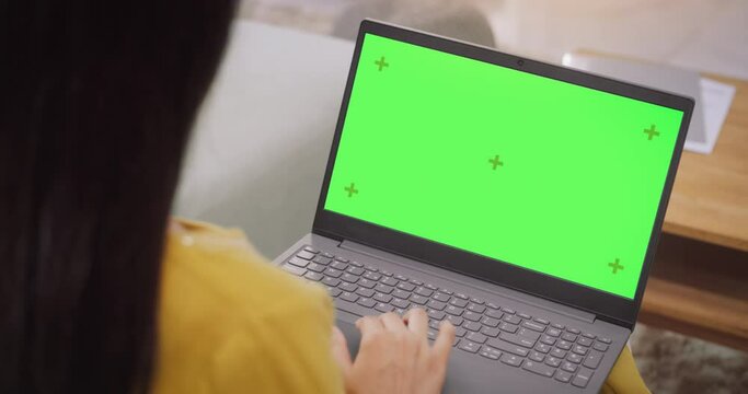 Over-the-Shoulder: Woman Using Laptop with Green Chroma Key Screen: Remote Work Collaboration, Video Conferencing. Browsing through Internet, Doing Online Shopping, Using Creative Software. Chroma Key