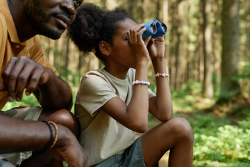 African American little girl looking through binoculars during hiking with her dad