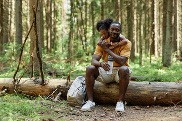 Portrait of African American family looking at camera while resting on log in the forest after hiking