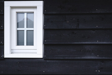 White window on the black wall of a wooden house