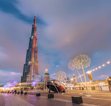 18 January 2023, Dubai, UAE: Famous Burj Khalifa skyscraper tower and illuminated dandelion sculptures at night on the promenade embankment in Dubai, UAE