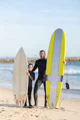 A family of surfers - father and son standing on the seashore with their surfing boards