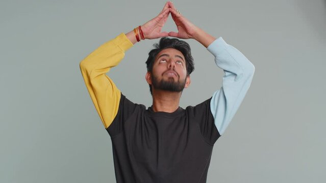 Young indian man playing childish catching up game, feeling in safe making roof above head with hands, insurance, security service. Bearded hindu guy isolated alone on gray studio background, indoors