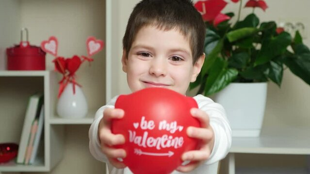 Cute 5 year old boy holds a balloon with the text be my valentine and smiles.