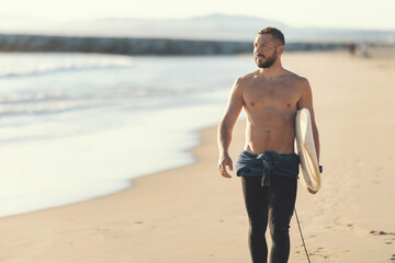 An athletic man surfer with naked torso walking on the seashore