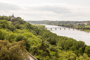 Fototapeta na wymiar Petit château sur une butte dominant un fleuve enjambé par un pont. Château de la Colinière à Champtoceaux, Orée d'Anjou, vue sur la loire.