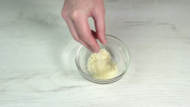 Hand takes a pinch of coconut flakes from a glass bowl, fingers sprinkle coconut flakes to decorate the dessert. Equipment for cooking. Kitchen utensils for baking, pastry and dessert