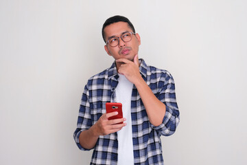 Adult Asian man holding mobile phone with suspicious expression