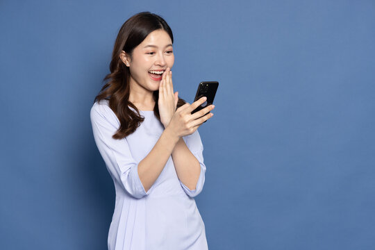 Happy Asian businesswoman typing or using mobile phone isolated on blue background