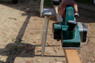 A manual electric plane on a rough log of a tree in the hands of a master. Wood products. Production of wood products.