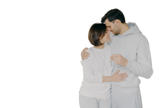 Lovely couple embrace and feel happy, holds keys from new modern first house, move in apartment for living together, pose in empty room with packed carton boxes, feel love to each other. Real estate - Powered by Adobe