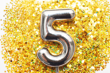 Five years birthday party. number five with golden confetti in form of stars on yellow background