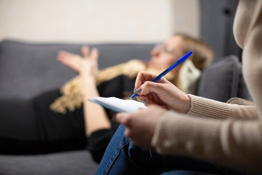 Female cient lying on couch shares childhood traumas with psychologist. Expert simultaneously records important details from patient life