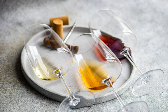 High angle of three varieties of Georgian dry wine glasses (white, amber and red) lying on a plate with a corkscrew and a cork on concrete grey table