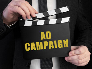 A businessman holds up a сlapperboard with text ad campaign