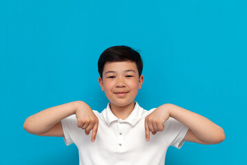 little asian boy in white t-shirt pointing down on blue background, korean kid advertising copy...