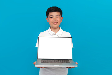 little asian boy showing blank laptop screen over blue background, korean kid advertising copy space