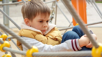 Upset and sad little boy being victim of bullying sitting alone on school playground. Child depression, problems with bullying, victim in school, emigration, criminal and poverty