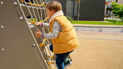Little boy climbing up the net at public playground. Active child, sports and development, kids playing outdoors.