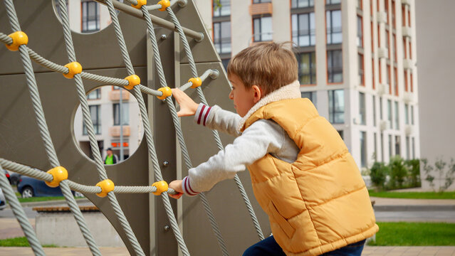 Little active boy climbing up the rope spider web on outdoor children playground on the sunny autumn day