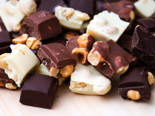 Heap of pieces of milk chocolate, white chocolate and dark chocolate with hazelnuts.