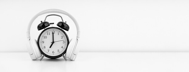 Black alarm clock with headphones on white wall background