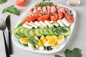 Healthy cobb salad with ham, feta cheese, cucumber, tomato, olives and eggs on white plate....