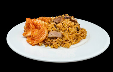 Homemade fried rice with sliced grilled lamb and kimchi on a white plate, isolated on black background.