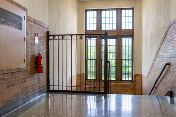 Nondescript stairway, hallway, with windows and brown railing, in a typical old US institutional building. 