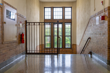 Nondescript stairway, hallway, with windows and brown railing, in a typical old US institutional building. 
