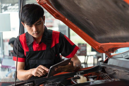 Young Asian male employee using computer to check engine operation, employee repairing engine, auto repair using diagnostic technology