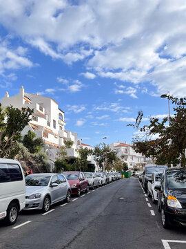 Many cars parked along the street with residential houses.