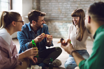Young happy friends having fun while eating pizza and drinking beer