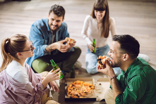 Young happy friends having fun while eating pizza and drinking beer