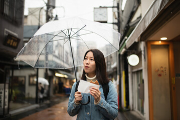 雨の日の商店街で食べ歩きをする女性