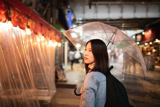 雨の日に夕暮れの繁華街を歩く女性