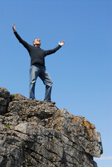 A man standing on a cliff with his arms raised to the blue sky